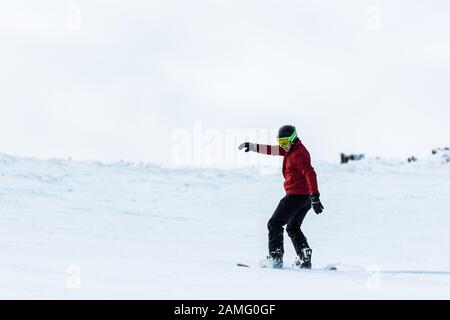 snowboarder athlétique dans le casque et les lunettes de protection qui se trouvent sur la pente à l'extérieur Banque D'Images