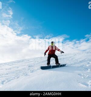 snowboarder en casque qui monte sur la pente contre le ciel bleu Banque D'Images