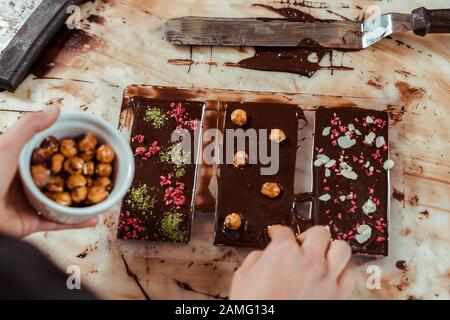 vue de dessus du chocolatier ajoutant des noisettes caramélisées dans un bar au chocolat noir Banque D'Images