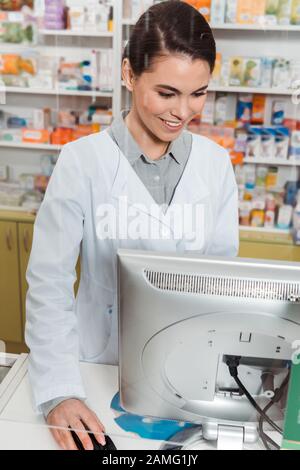 Pharmacien souriant attrayant utilisant l'ordinateur en pharmacie Banque D'Images