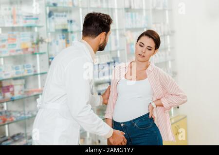 Le drogiste aidant la femme enceinte avec la pharmacie vitrine à l'arrière-plan Banque D'Images