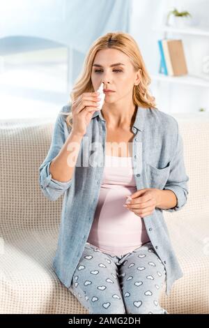 femme enceinte malade utilisant un jet nasal tout en étant assise sur le canapé Banque D'Images