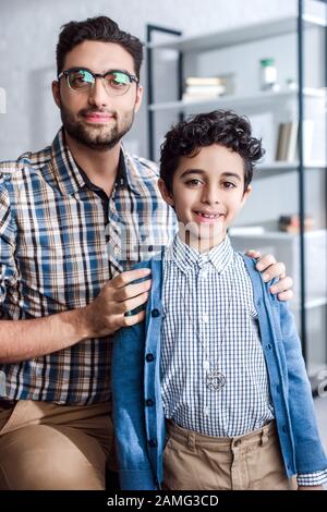 un père juif souriant embrassant son fils et regardant l'appareil photo dans l'appartement Banque D'Images