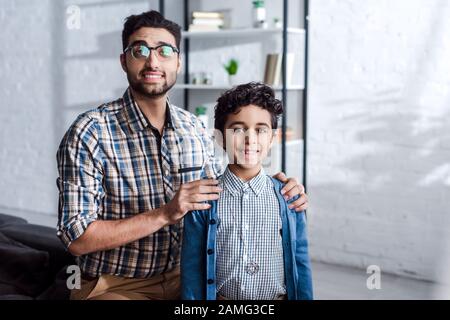 un père juif souriant embrassant son fils et regardant l'appareil photo dans l'appartement Banque D'Images