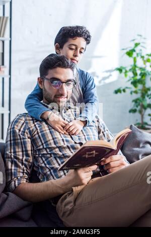 père juif souriant et fils lisant tanakh dans l'appartement Banque D'Images