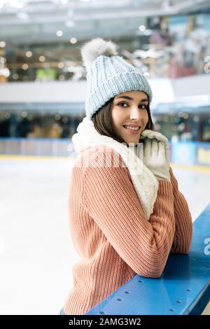 belle fille souriante en sweat-shirt, écharpe, gants et chapeau debout sur la patinoire Banque D'Images