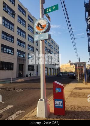 À l'angle de la 44ème rue et du boulevard Vernon, à long Island City, Queens, 11 mars 2019. Boîte à journaux et arrêt de bus Am NY au coin de la rue. Le panneau de l'ère des années 1990 sur le poteau de lampe annonçant le projet d'art 'Randonnée New York long Island City', avec des distances de marche aux attractions locales imprimées ci-dessous. De l'autre côté de la rue se trouve un bâtiment New-yorkais de Dept of Education au 44-36 Vernon Blvd avec une façade datant des années 1930 intitulée « City of New York, Dept of Purchase, Bureau of Stores ». () Banque D'Images