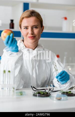 foyer sélectif du biologiste souriant tenant la pomme entière et le tube à essai en laboratoire Banque D'Images