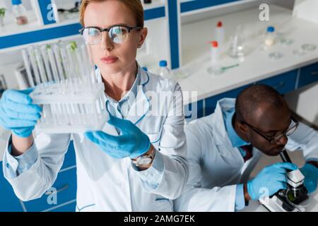 vue à grand angle du biologiste regardant les tubes à essai et le collègue afro-américain au microscope Banque D'Images