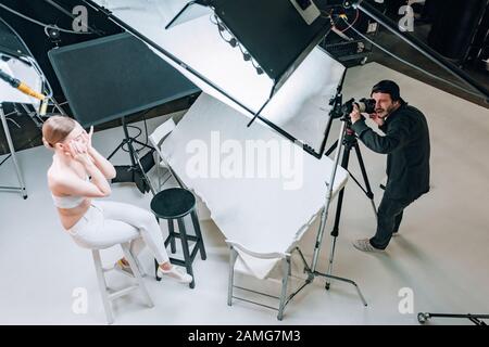 Vue en hauteur du magnifique modèle et du vidéaste travaillant en studio photo avec des spots Banque D'Images