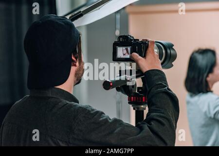 Vue arrière du vidéaste avec assistant et modèle de travail en studio photo Banque D'Images
