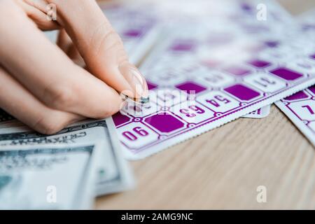 vue rognée d'une femme tenant une pièce de monnaie et grattant un billet de loterie sur la table Banque D'Images