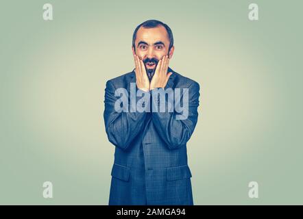 Heureux adulte beau homme regardant choqué surpris par l'incrédulité des mains sur les yeux de la bouche ouverte large de joue, isolé vert clair fond de mur jaune. Posi Banque D'Images