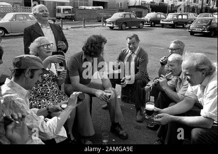 Années 1970 Royaume-Uni, groupe de travailleurs de bureau et d'usine profiter de leur voyage annuel en autocar au bord de la mer. Ils apportent leur propre bière et sont dans le parking Southend on Sea. Un homme joue sur un sifflet de Penny. Tandis que d'autres sup leurs pintes (ils sont assis sur des caisses de bière) Southend on Sea Essex England 1974 HOMER SYKES Banque D'Images