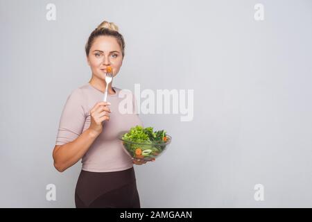 Portrait d'une femme à la coupe attrayante avec un pain à cheveux tenant un bawl de salade de légumes frais et regardant l'appareil photo, régime végétarien, nourriture saine, espace de copie Banque D'Images