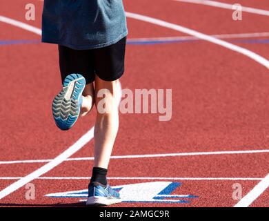 Vue arrière d'un jeune coureur masculin dans la voie quatre sur une voie rouge avec des chiffres blancs avec une bordure bleue. Banque D'Images