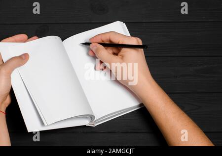 Les mains des hommes tiennent un carnet blanc avec des pages propres et un crayon noir Banque D'Images