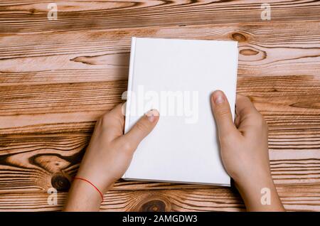 Les mains des hommes tenant un livre fermé avec une couverture vierge sur fond clair Banque D'Images