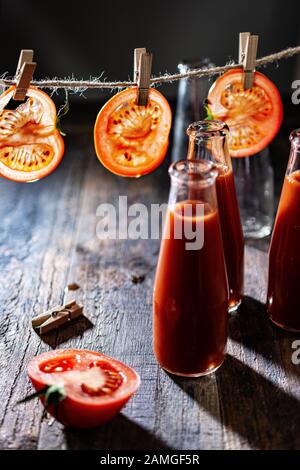 Tranches de tomate accrochées sur une chaîne.jus de tomate dans des bouteilles de verre.boisson Fraîche et nourriture. Banque D'Images