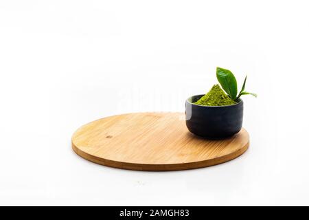 Isolez la poudre de thé vert tas dans un bol en céramique noire. Extraire Les Feuilles de thé dans une tasse en pierre sombre. Avec Mini feuilles de thé vert sur une plaque en bois vierge. Banque D'Images