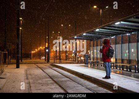 L'homme en manteau d'hiver rouge debout à l'arrêt de tramway bus en attente pour les transports publics Banque D'Images