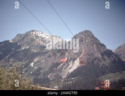 Photographie vernaculaire prise sur un film analogique de 35 mm transparent, considérée comme représentant une montagne brune et blanche sous le ciel bleu pendant la journée avec un téléski ou une télécabine, 1965. Les Principaux Sujets/Objets Détectés Sont Les Paysages Montagneux, La Montagne, Le Ciel, La Chaîne De Montagnes, La Colline, L'Arbre, La Vallée, Le Paysage, L'Hiver, Le Tourisme, La Roche, La Neige, La Nature Et La Couleur Grise. () Banque D'Images