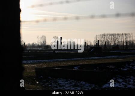 Auschwitz- Birkenau, Pologne- clôture électrique avec fil barbelé, casernes détruites, chambres à gaz et cheminées de crématorium en brique dans le camp de concentration Banque D'Images