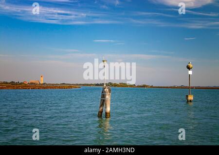 Des colonnes en bois dans l'eau marquent le chemin du bateau entre les îles de Burano, Murano et Venise, Italie. Le mouette est assis sur le pilier. Banque D'Images