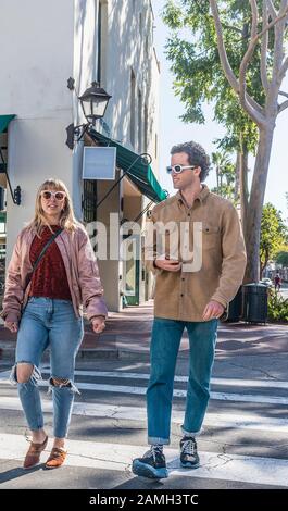 Un couple de hanche marchant sur le trottoir à Santa Barbara, en Californie, arborant ses lunettes de soleil à la mode, et son Jean déchiré. Banque D'Images