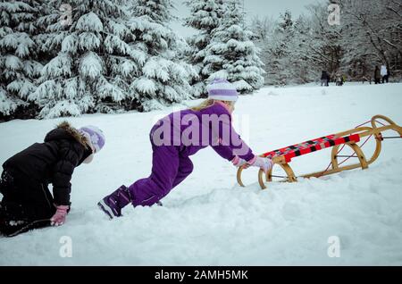 deux belles petites filles qui courent en traîneau dans la forêt d'hiver avec beaucoup de neige Banque D'Images