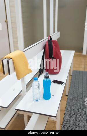 Sac à dos, bouteilles, serviette et téléphone sur un banc en bois dans un vestiaire. Banque D'Images