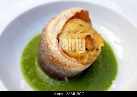 Bar de mer avec sauce aux pois, servi dans une assiette blanche. Menu du restaurant italien. Bar de mer cuit au four et préparé dans une spirale sur une purée de pe vert Banque D'Images