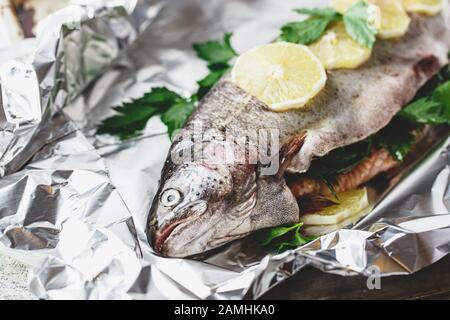 Truite arc-en-ciel fraîche avec persil et citron en feuille d'aluminium sur fond gris clair. Des aliments sains. Concept de cuisson. Gros plan. Banque D'Images