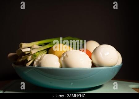 Ingrédients pour la salade - œufs durs, pommes de terre, carottes et oignons verts sur une plaque bleue avant de trancher Banque D'Images