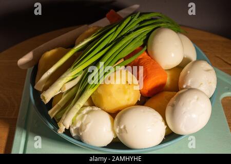 Ingrédients pour la salade - œufs durs, pommes de terre, carottes et oignons verts sur une plaque bleue avant de trancher Banque D'Images