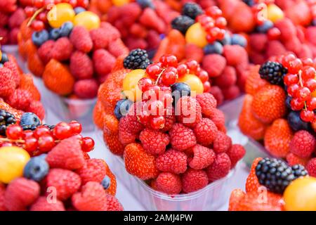 Punets en plastique de framboises, fraises, groseilles, mûres, physalis et autres fruits à vendre dans une boutique de fruits. Banque D'Images