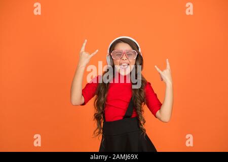 Piste froide. Événement et divertissement. Fille de fête. Accessoire de fête. Amuse-toi bien. Liste de lecture pour la fête. Concept de musique. Enfant porter des lunettes. Magasin de mode de lunettes. Fille avec lunettes arrière-plan orange. Banque D'Images