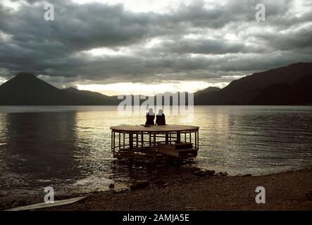 Silhouette d'un couple assis sur une jetée, en regardant le coucher de soleil spectaculaire au lac Atitlan, Panajachel, Guatemala. Déc 2018 Banque D'Images