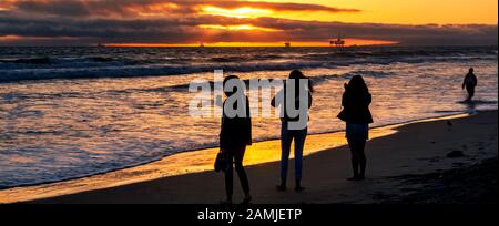Coucher de soleil animé sur la plage. Silhouettes de trois femmes photographiant un coucher de soleil flamboyant avec leurs téléphones cellulaires au bord de l'eau à Huntington Beach. Banque D'Images