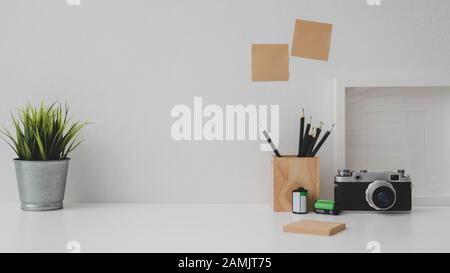 Prise de vue rognée de l'espace de travail du photographe avec espace de copie, appareil photo, papeterie, cadre de maquette et potentiomètre d'arbre sur une table blanche avec fond de mur blanc Banque D'Images