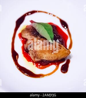 Foie gras poêlé sélectif Concentré avec décoration de sauce aux baies servie sur une plaque en porcelaine blanche. Foie De Canard Ou D'Oie Engraissé Comme Delica Alimentaire Français Banque D'Images