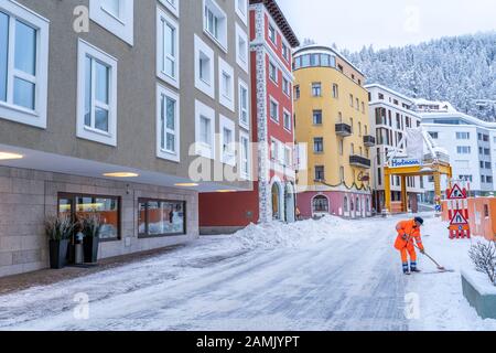 Saint-Moritz, Suisse - 22 décembre - un agent de nettoyage de route en manteau orange brillant élimine la neige de la route dans une rue de Saint-Moritz, Suisse Banque D'Images