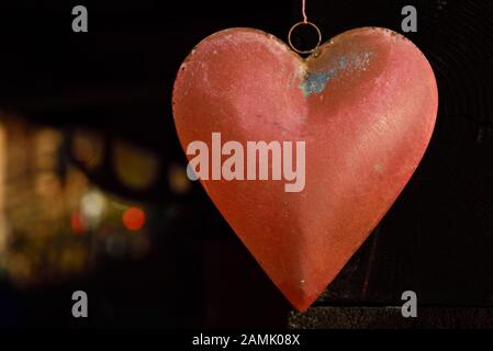 Un vieux coeur métallique avec de la peinture rouge et des traces d'utilisation et de l'altération se bloque sur un fond sombre avec de la lumière dans l'arrière-plan Banque D'Images