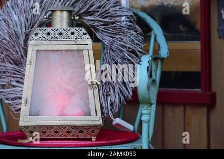 Noël et hiver encore la vie avec une ancienne lanterne romantique, qui a des panneaux glacés congelés, sur une chaise devant une porte en bois avec une couronne Banque D'Images