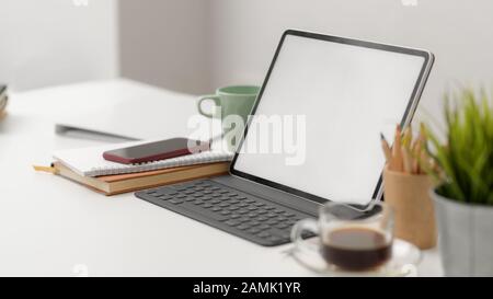 Photo rognée d'un espace de travail simple avec un ordinateur portable à écran vide, des crayons de couleur, un smartphone, un pot d'arbre et des fournitures de bureau sur fond de table blanc Banque D'Images