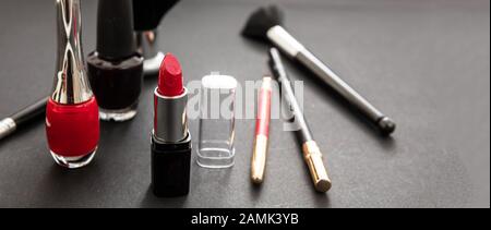 Maquillage produits cosmétiques en rouge et noir. Rouge rouge rouge à lèvres et vernis à ongles, crayon pour les yeux et pinceaux sur fond noir Banque D'Images