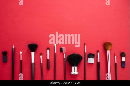 Créez des brosses sur fond rouge, vue du dessus. Outils professionnels pour le maquillage et l'art, salon de beauté, concept cosmétique Banque D'Images