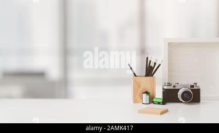 Prise de vue rognée de l'espace de travail du photographe avec espace de copie, appareil photo, papeterie, cadre de maquette et potentiomètre d'arbre sur une table blanche avec arrière-plan flou Banque D'Images