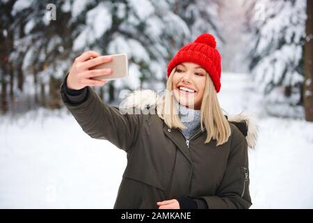 Femme souriante qui fait du selfie dans la forêt d'hiver Banque D'Images