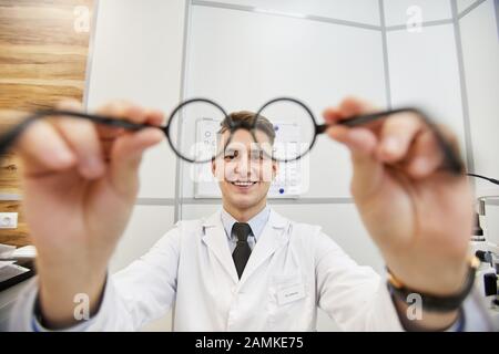 Prise de vue de jeune optométriste souriant mettant des lunettes sur un patient non reconnaissable pendant le test de vision dans une clinique moderne, espace de copie Banque D'Images